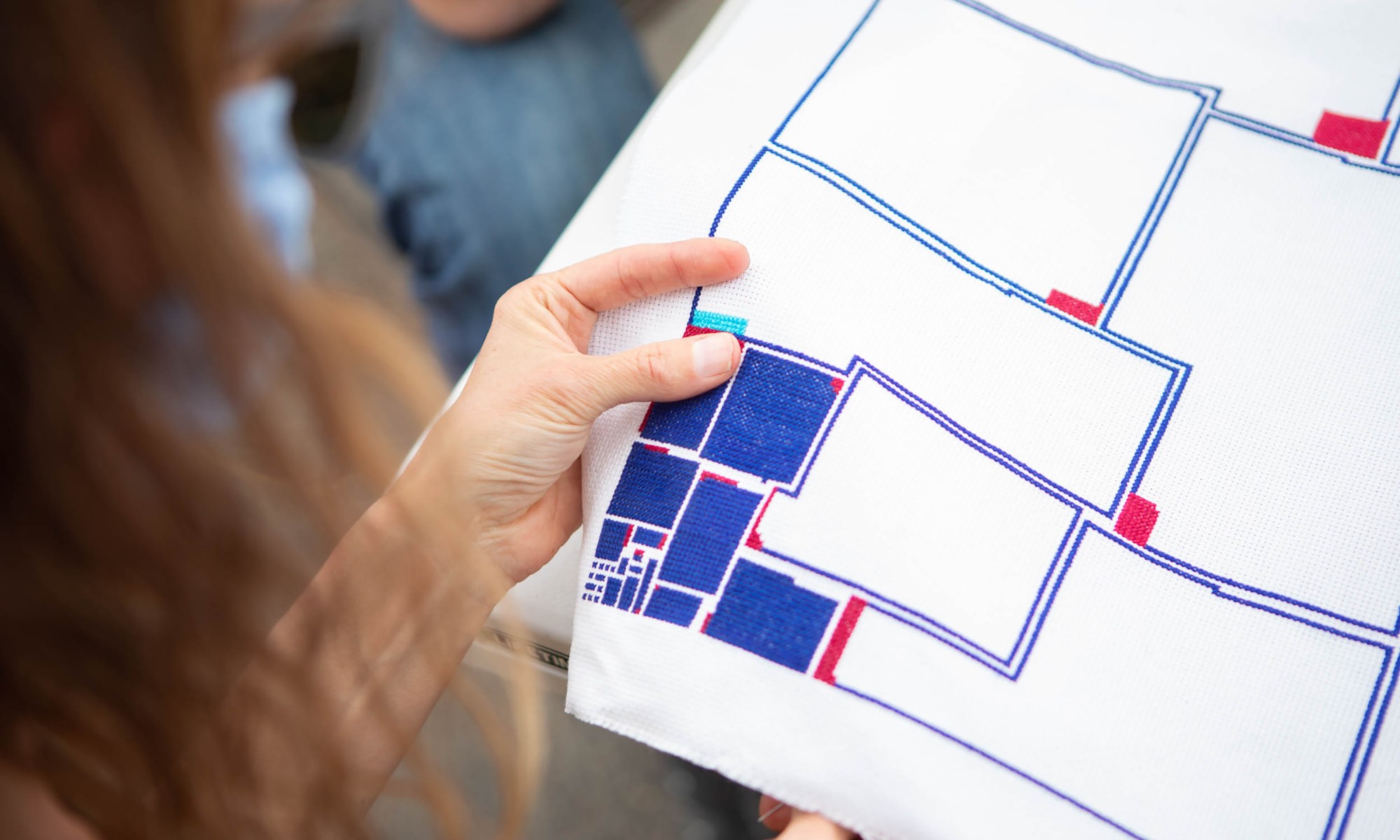 hands holding a geometric cross-stitch embroidery