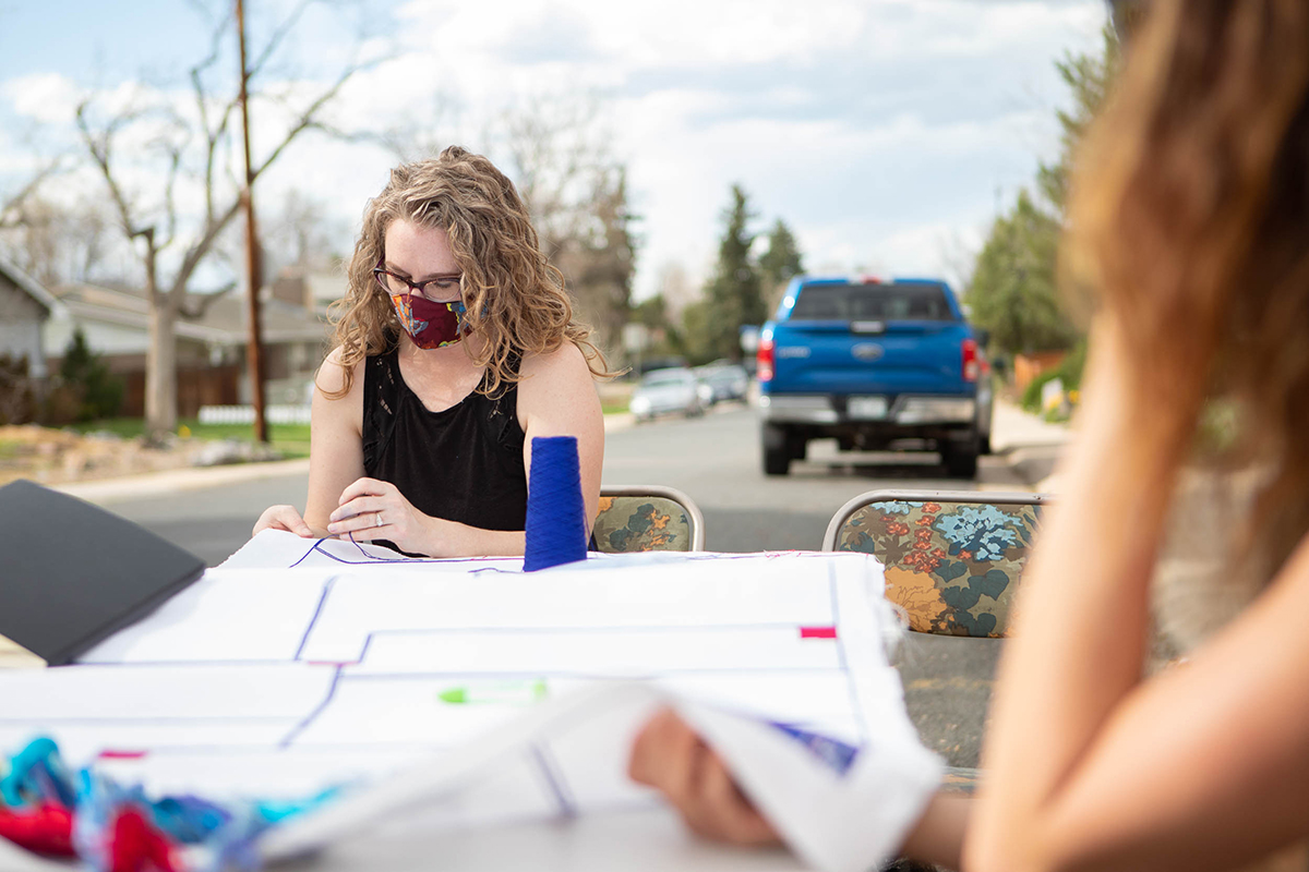 woman sitting at a table on the street, stitching a large cloth