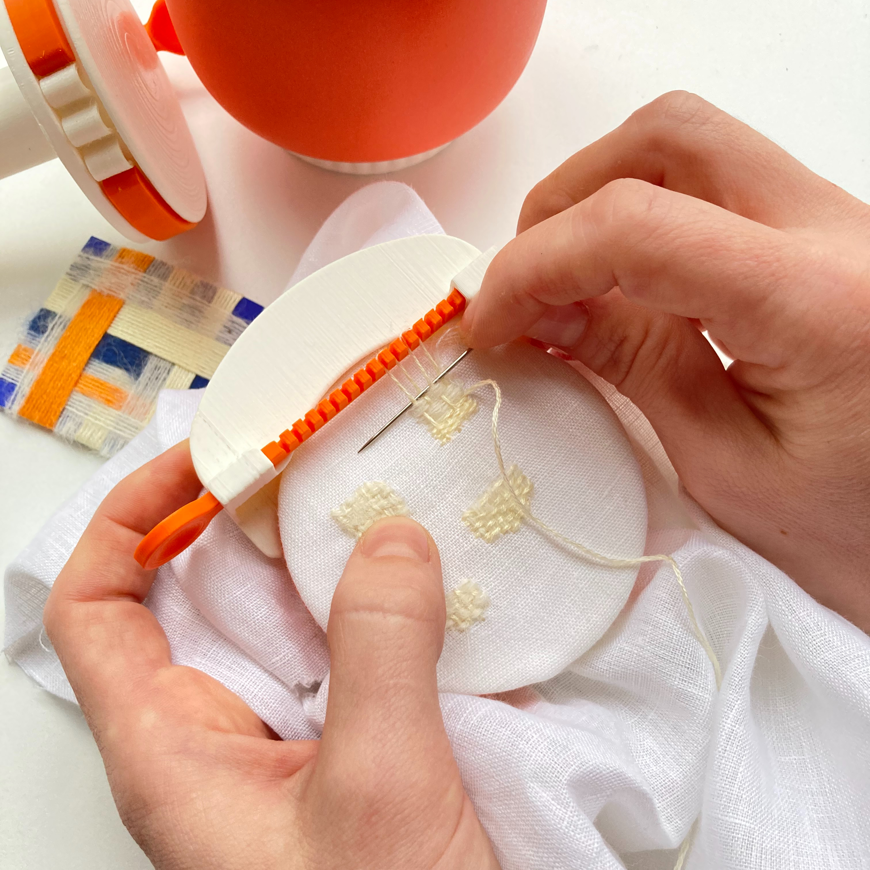 hands holding fabric, a needle and a tool that is holding threads to enable a darn to be stitched